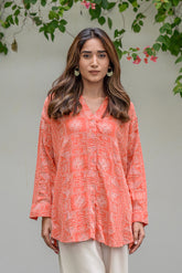 Woman wearing a coral patterned blouse with white pants against a natural background