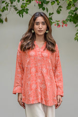 Woman wearing a coral patterned blouse with white pants against a natural background