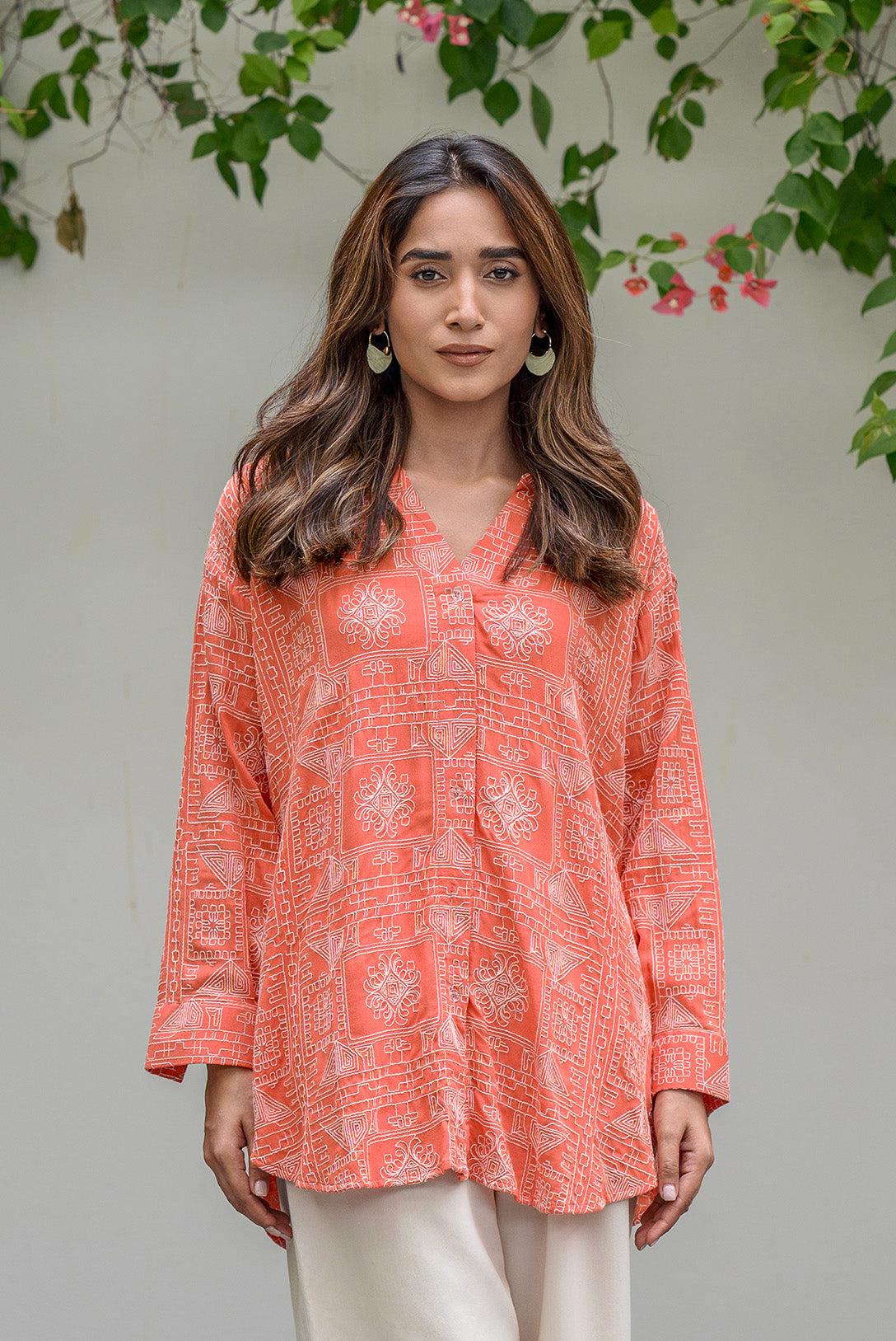 Woman wearing a coral patterned blouse with white pants against a natural background