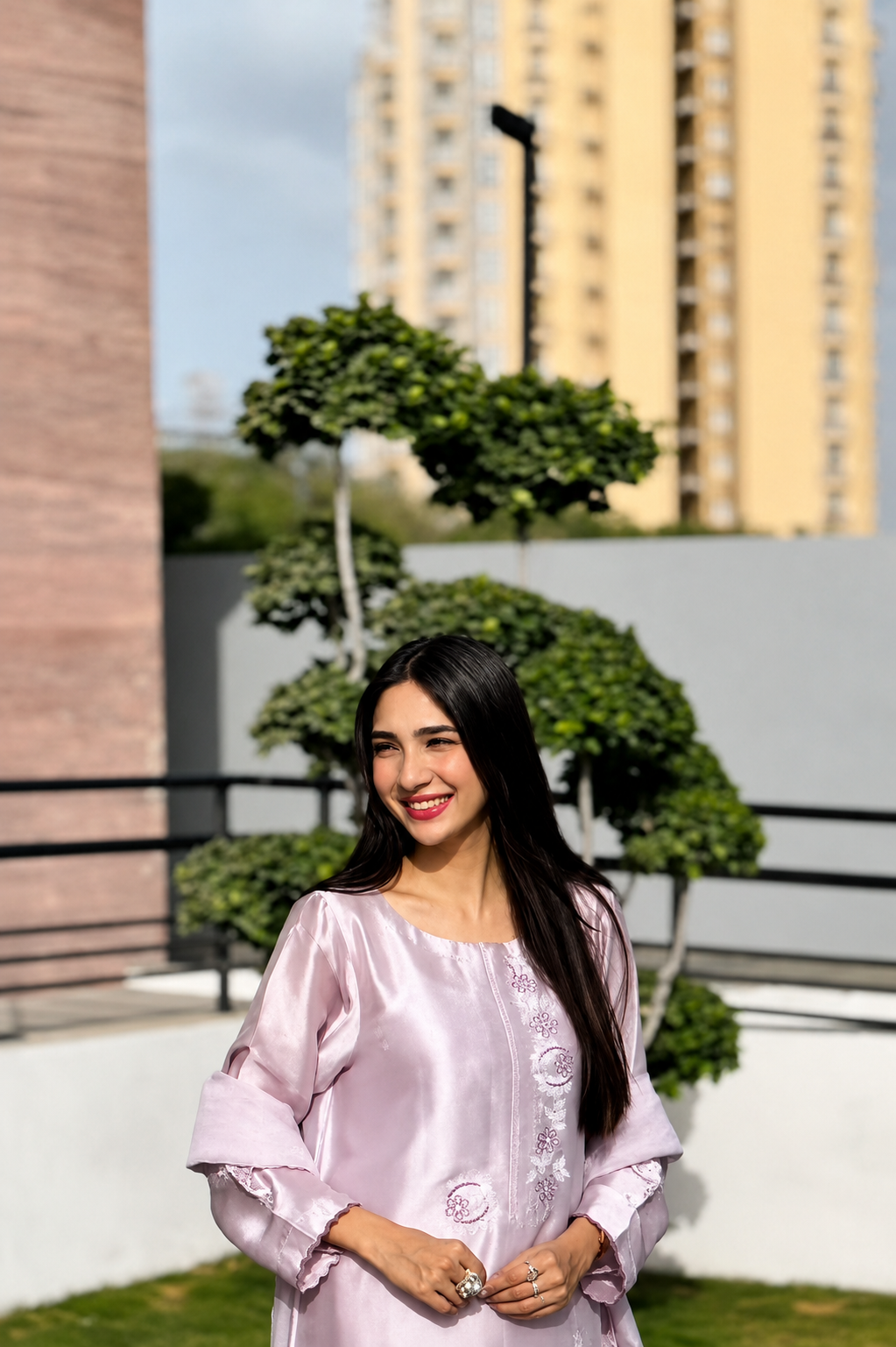 Woman in a light purple dress standing outdoors with buildings and greenery in the background