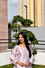 Woman in a light purple dress standing outdoors with buildings and greenery in the background