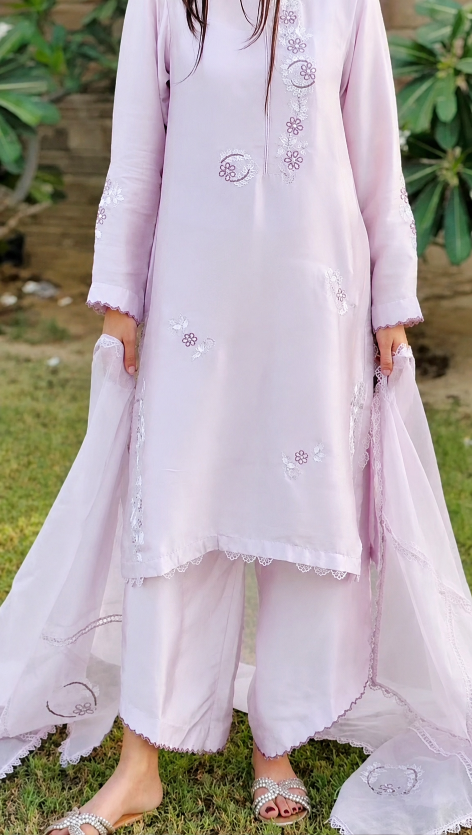 Person wearing a lilac traditional outfit with floral embroidery in a natural setting.